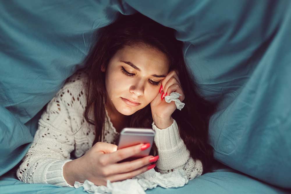 young girl sad on her phone under the covers