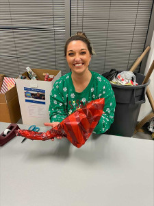 volunteer holding a wrapped present at company Holiday Heroes wrapping party