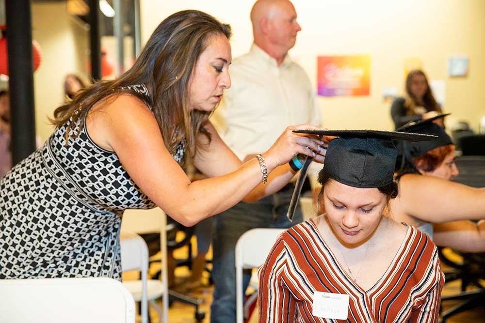 Job prep volunteer, Lelani, putting a graduation cap on young woman's head